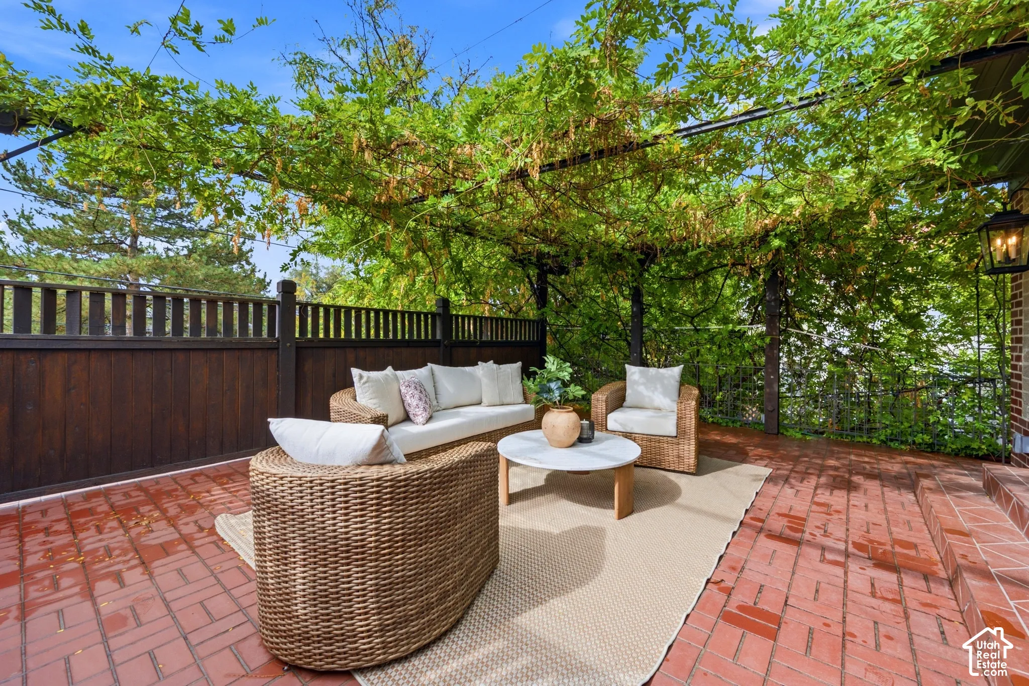 Brick paver patio with a vine-covered pergola, adjacent to a dark wood privacy fence, and antique style lanterns