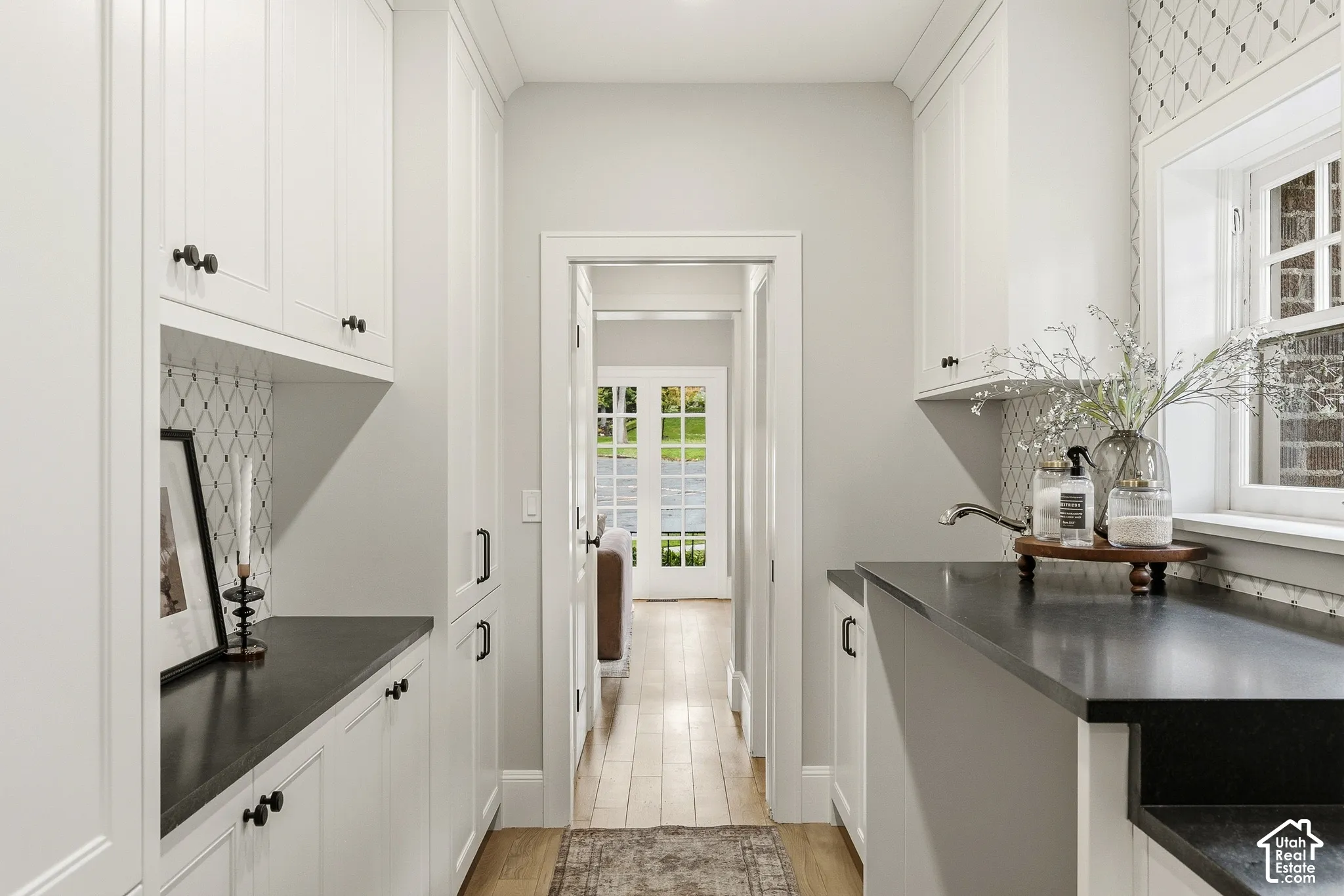 White cabinetry with bronze hardware, dark countertops, a window with exterior brick detail, and wood-finish flooring