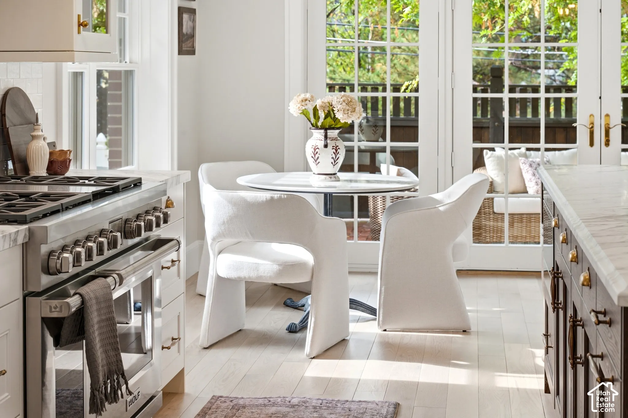 Professional-grade stainless steel range with gas cooktop, light wood-finish flooring, white stone countertops, dark wood cabinetry with brass hardware, and double French doors with transom windows