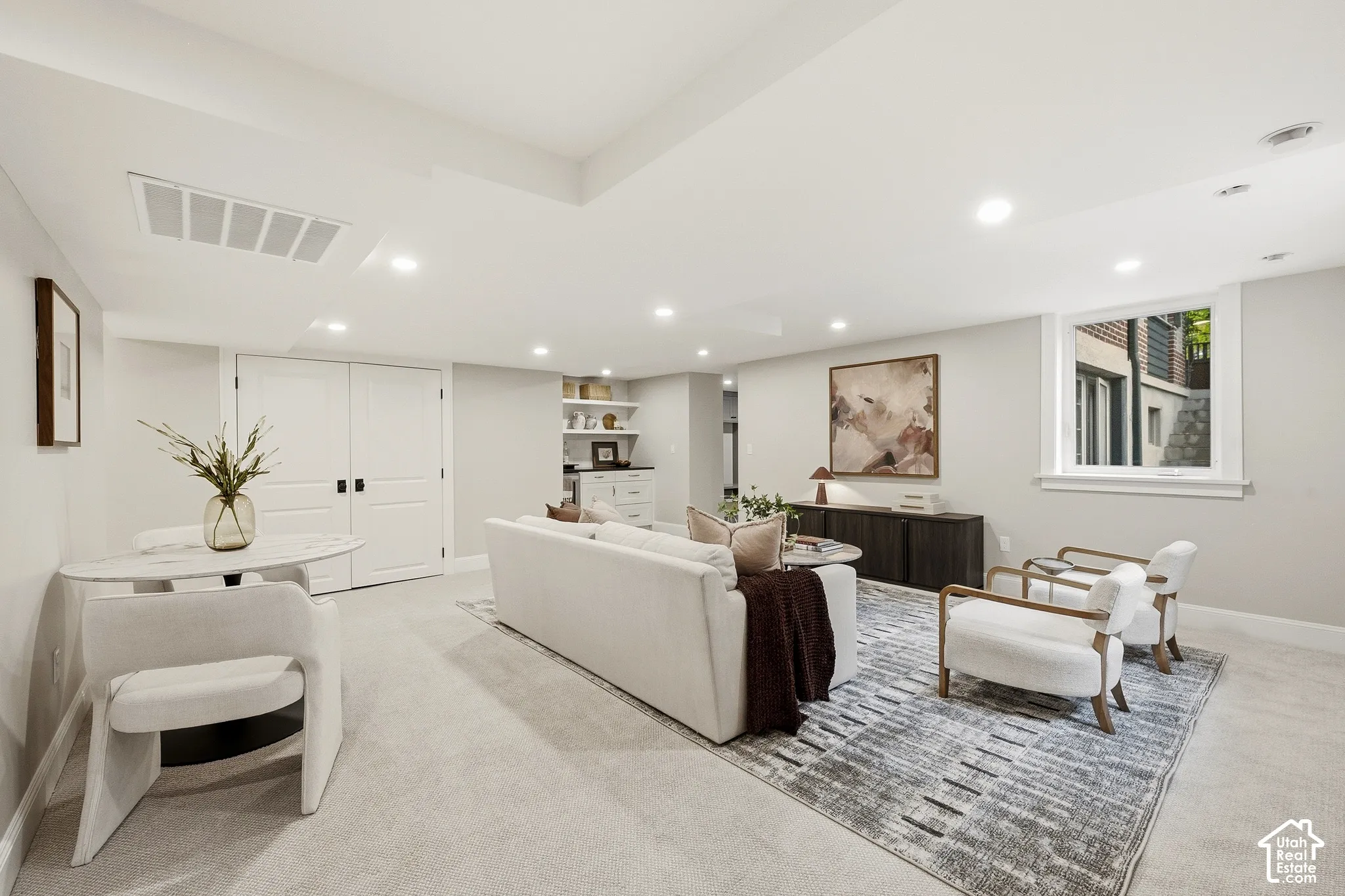 Recessed lighting, light-colored carpeting, built-in shelving, white double doors, and a window providing natural light to the backyard
