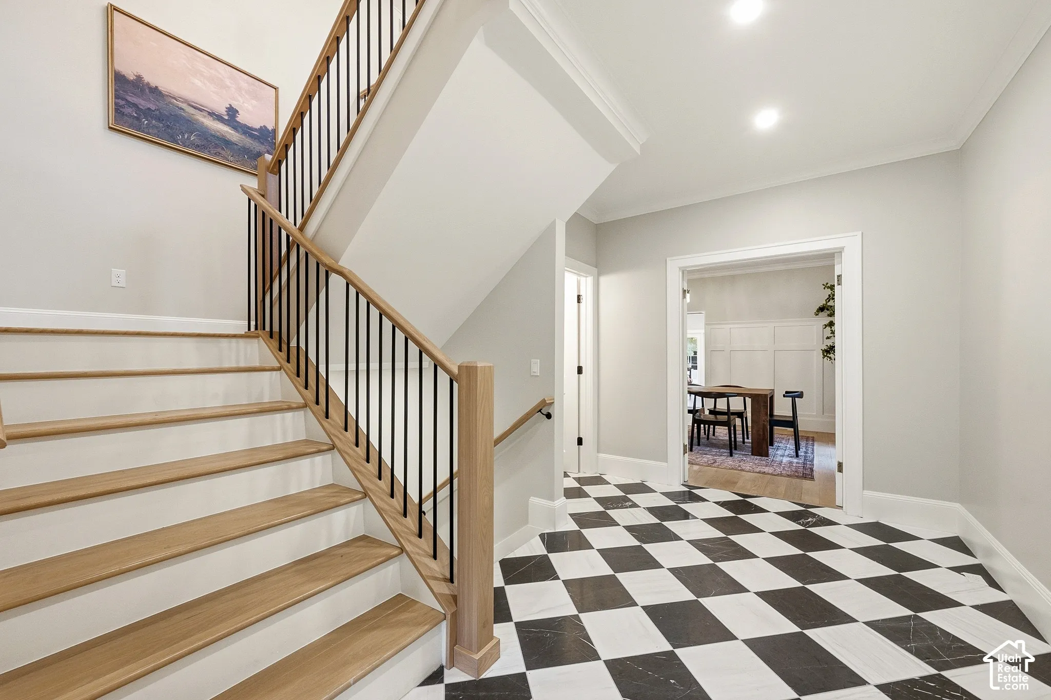 Checkered floor tiling, wood-finish staircase, black metal balusters, and recessed ceiling lighting, with view towards formal dining room