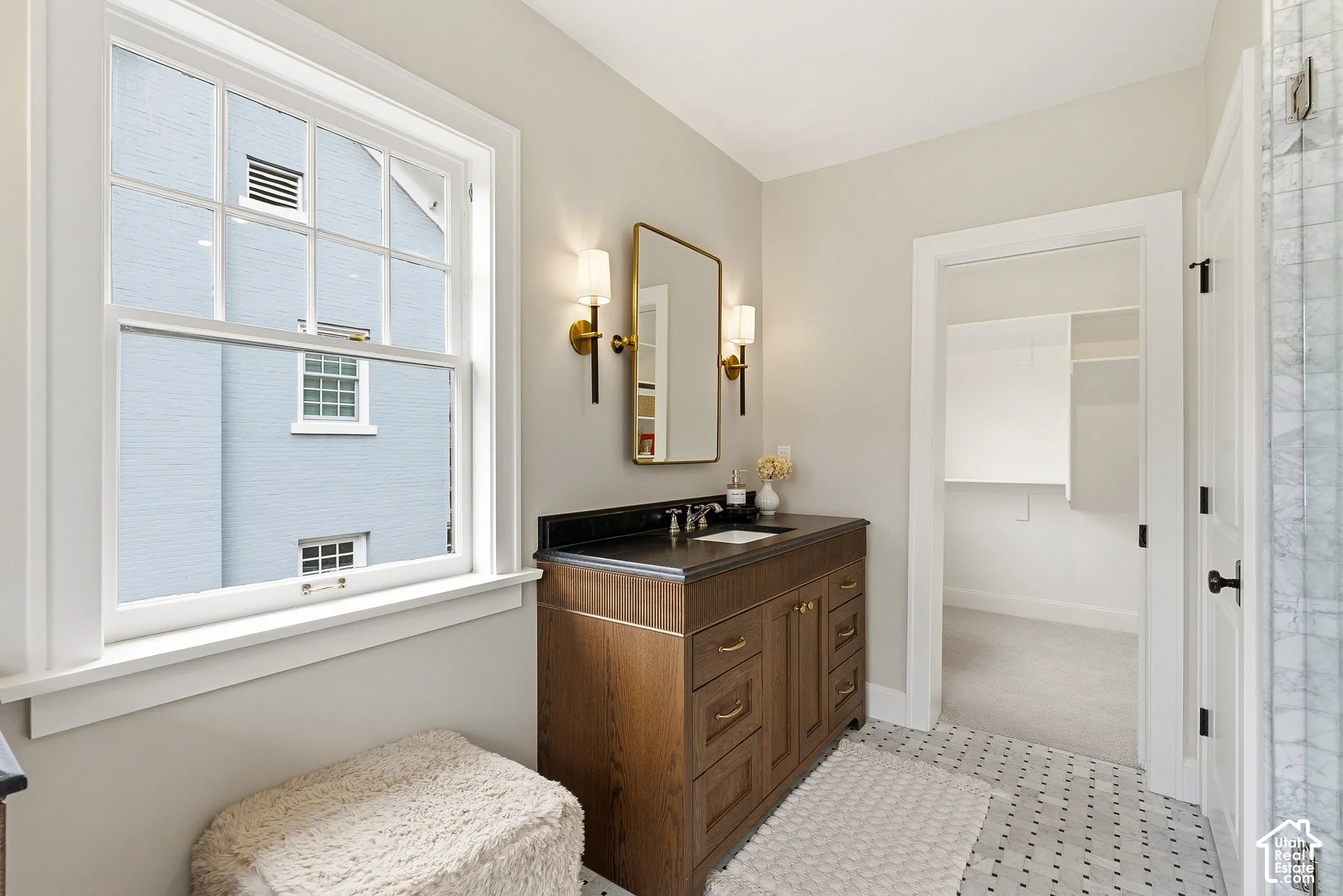 Primary Bath. Wood-finish vanity with dark countertop, rectangular sink, and brass-tone sconces