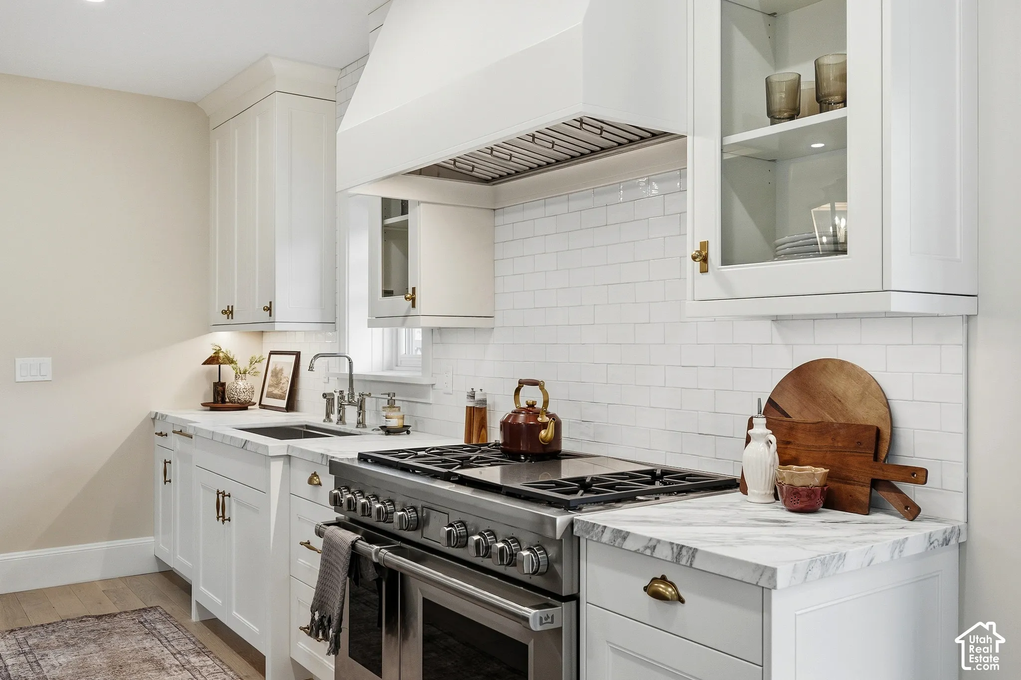 White shaker-style cabinetry with brass hardware, honed marble countertops, Wolf 48" stainless steel dual fuel range with a ventilation hood, subway tile backsplash, and a stainless steel sink with a polished nickel faucet
