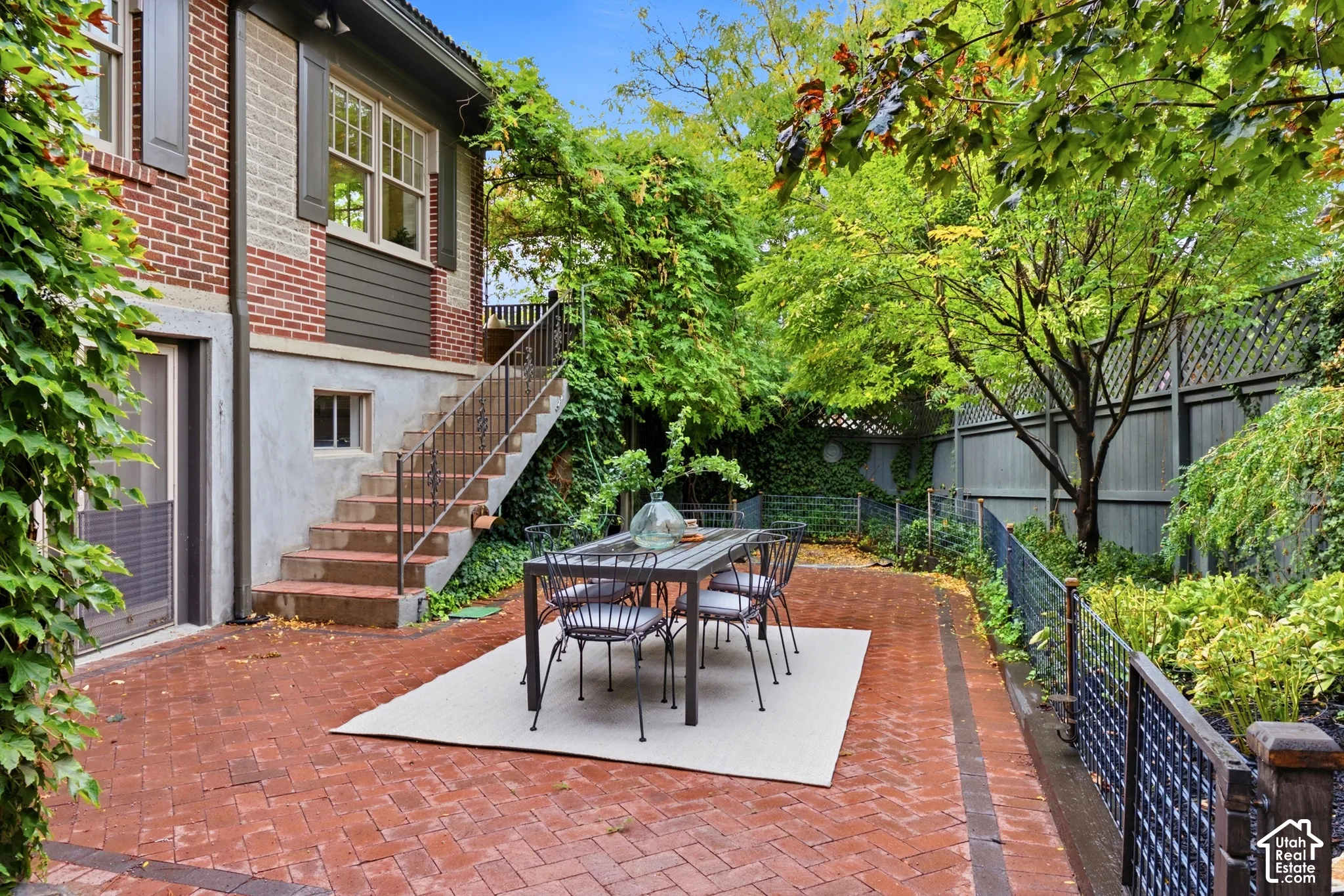 Brick paver patio with a surrounding garden, mature trees, and a decorative fence
