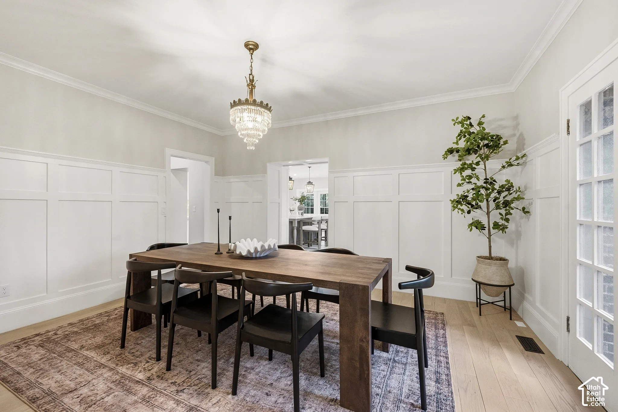 White paneling with crown molding, wood-finish flooring, original crystal chandelier, and French doors
