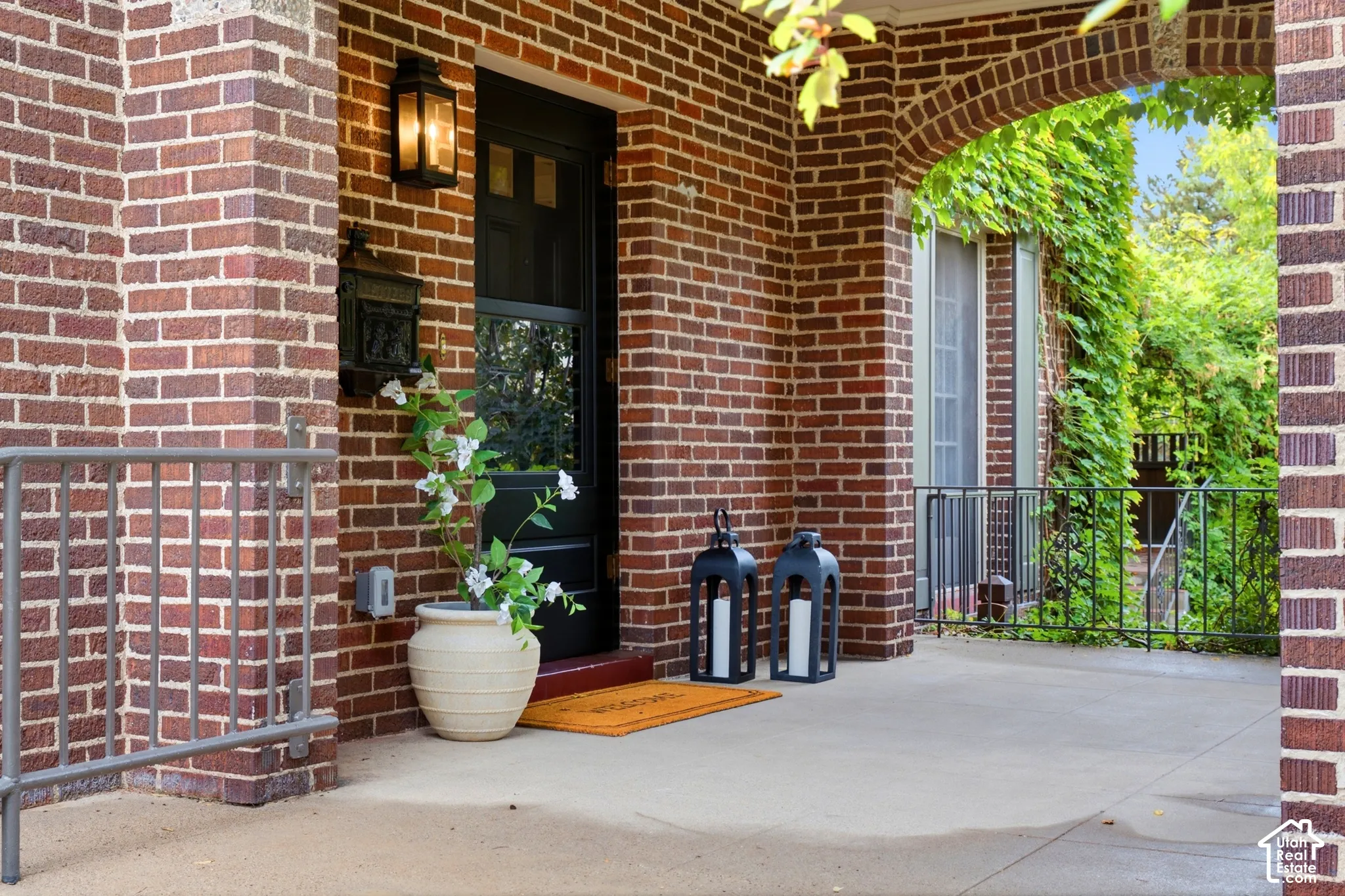 Brick exterior with a dark-paneled door, exterior wall lantern, and concrete porch