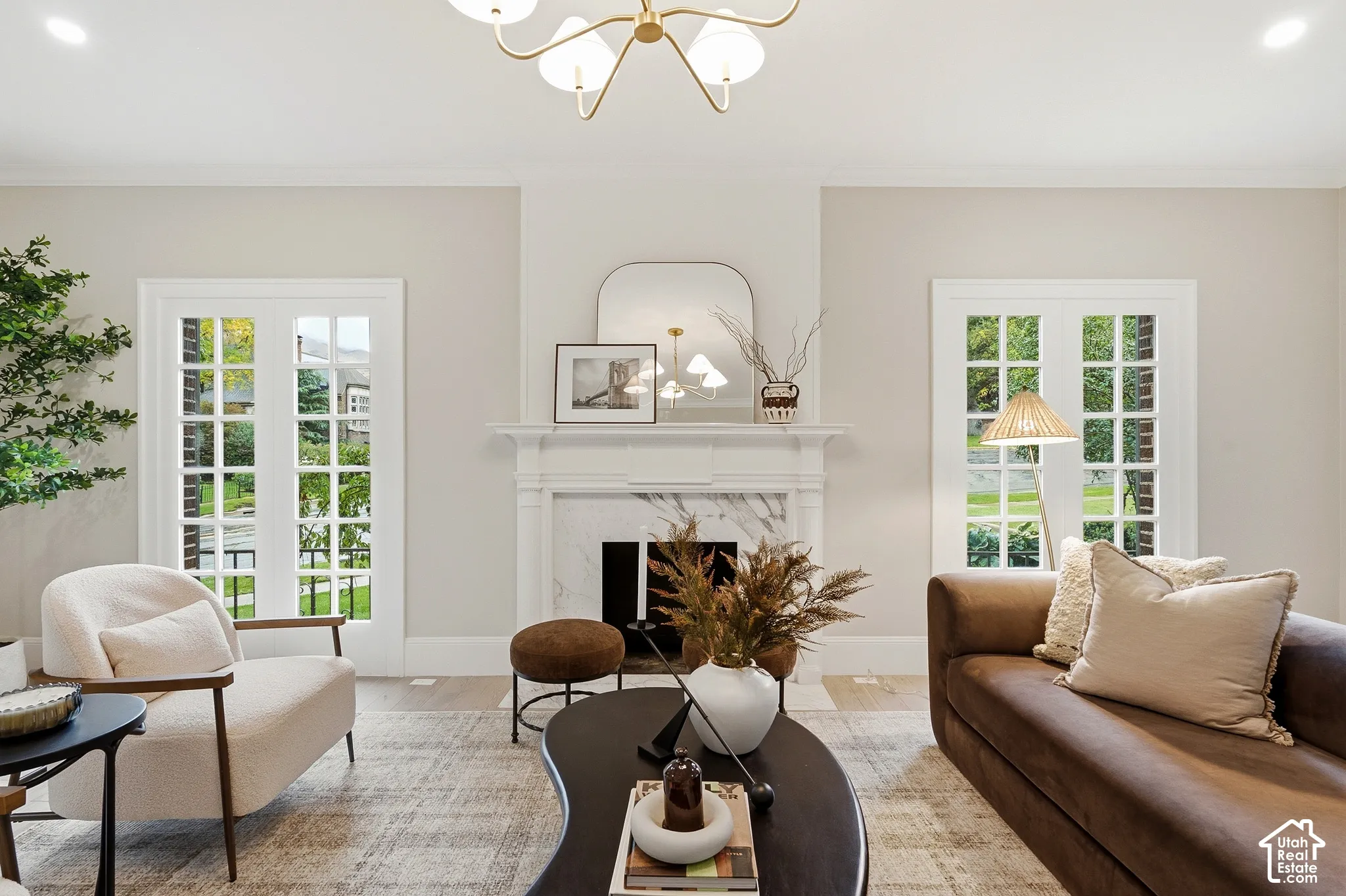 Spacious living area featuring a decorative fireplace with a marble surround, dual French doors, a prominent chandelier, and light wood-finish flooring