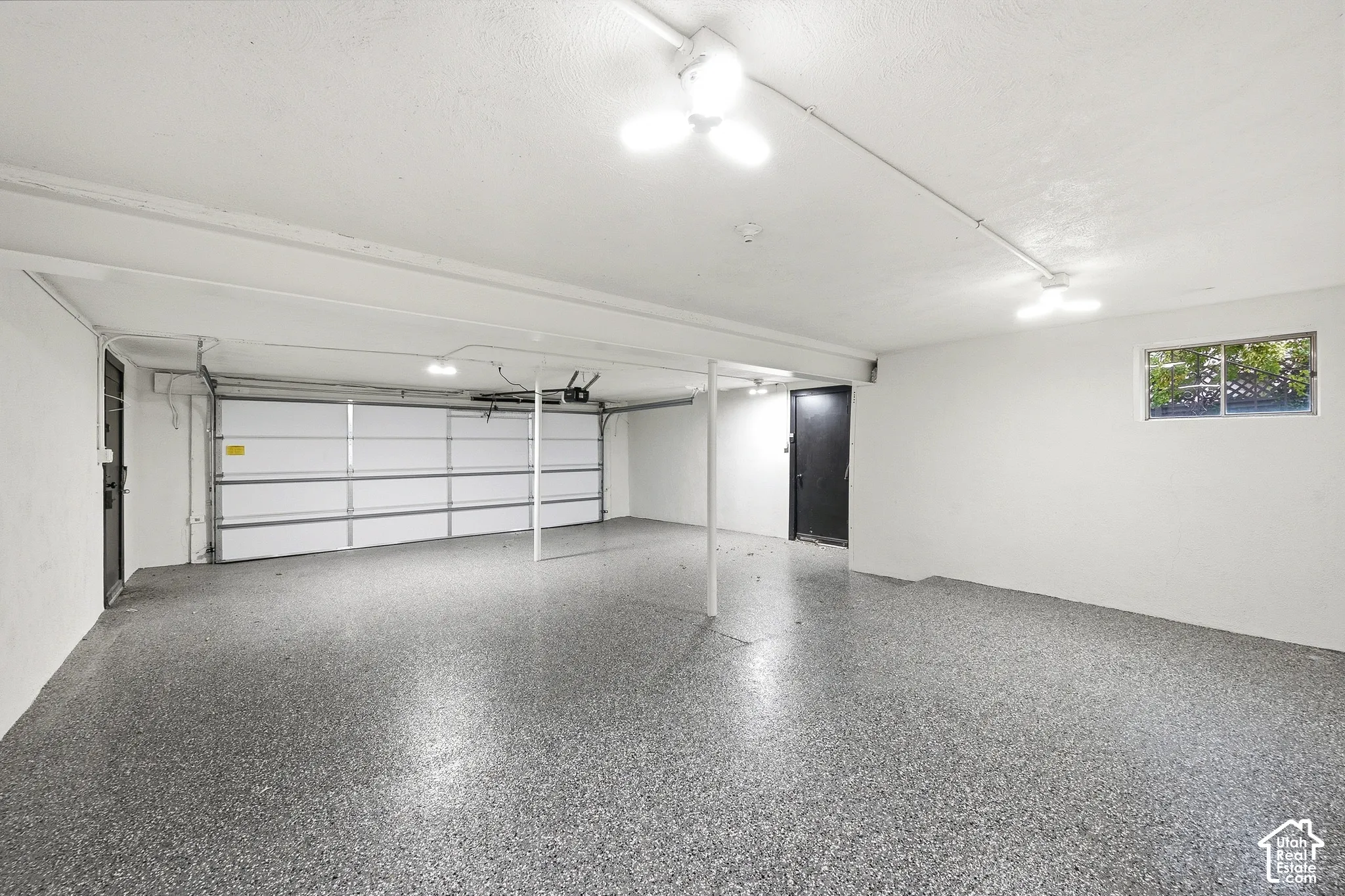 Spacious garage with an overhead door, light gray speckled flooring, white walls, and a single window