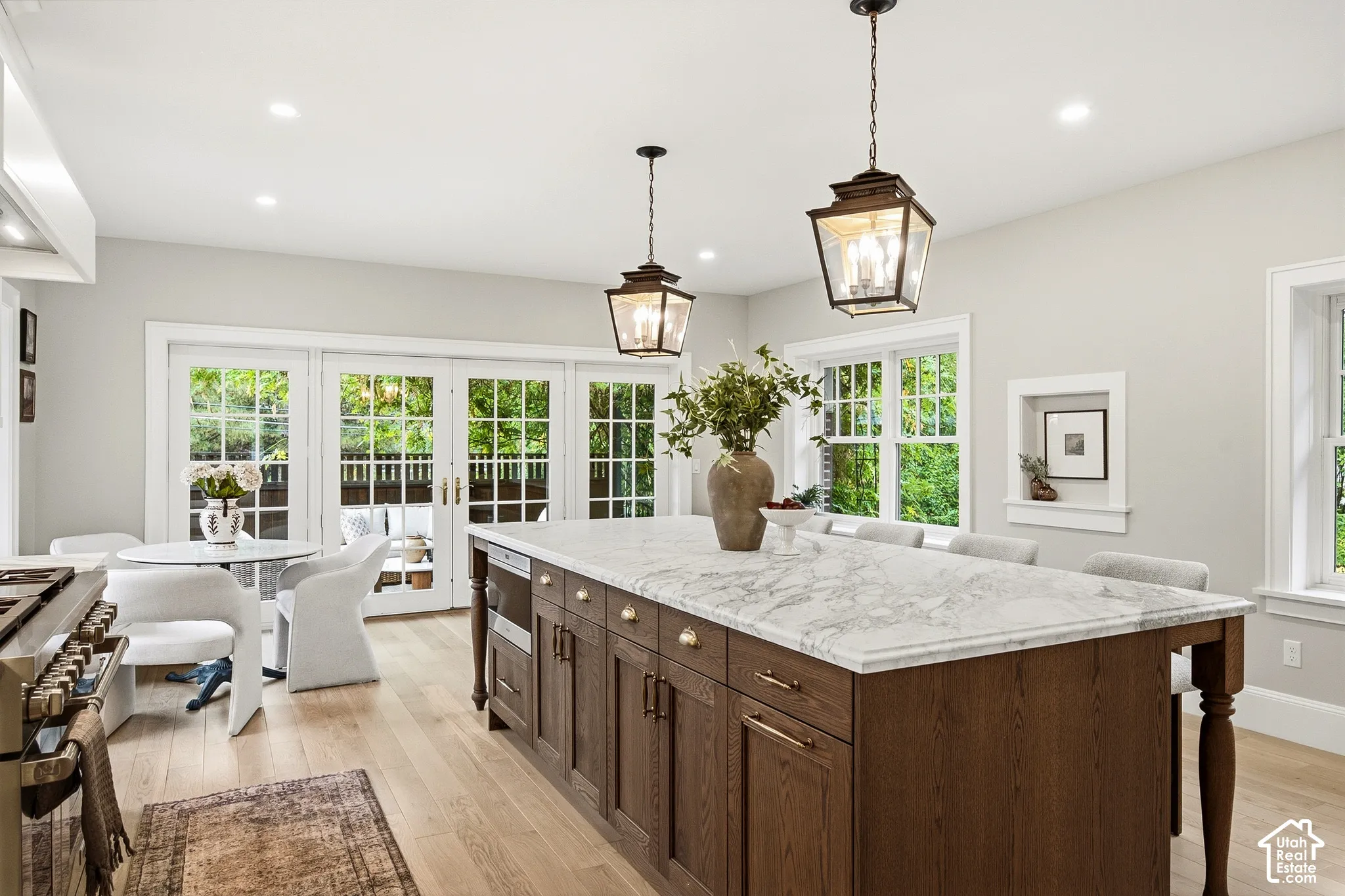 Expansive kitchen island with a stone countertop, recessed lighting, wood-finish flooring, and multiple windows facing an upper level patio seating area