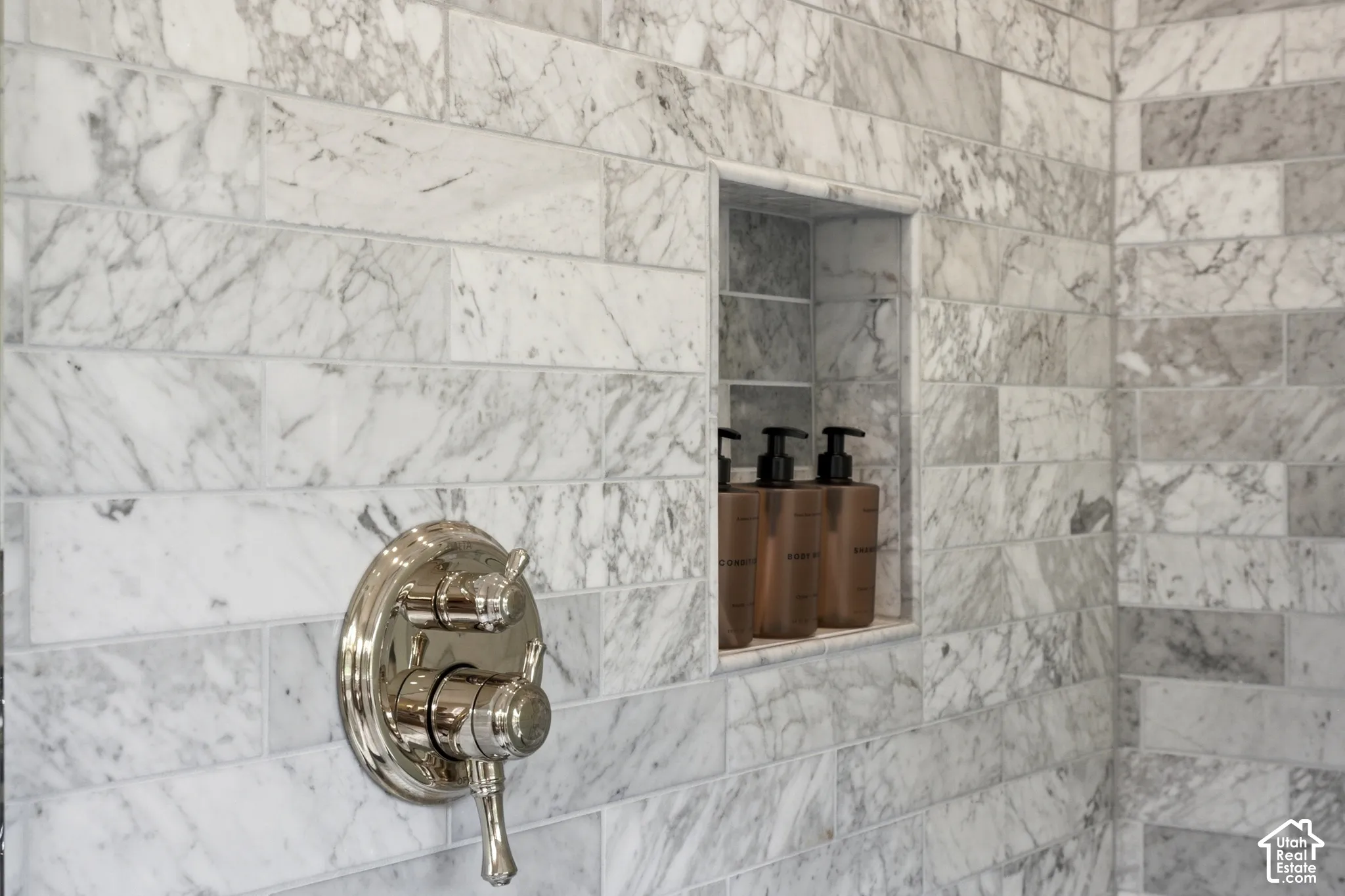 Marble-tiled shower surround with a polished nickel shower control and built-in recessed shelving