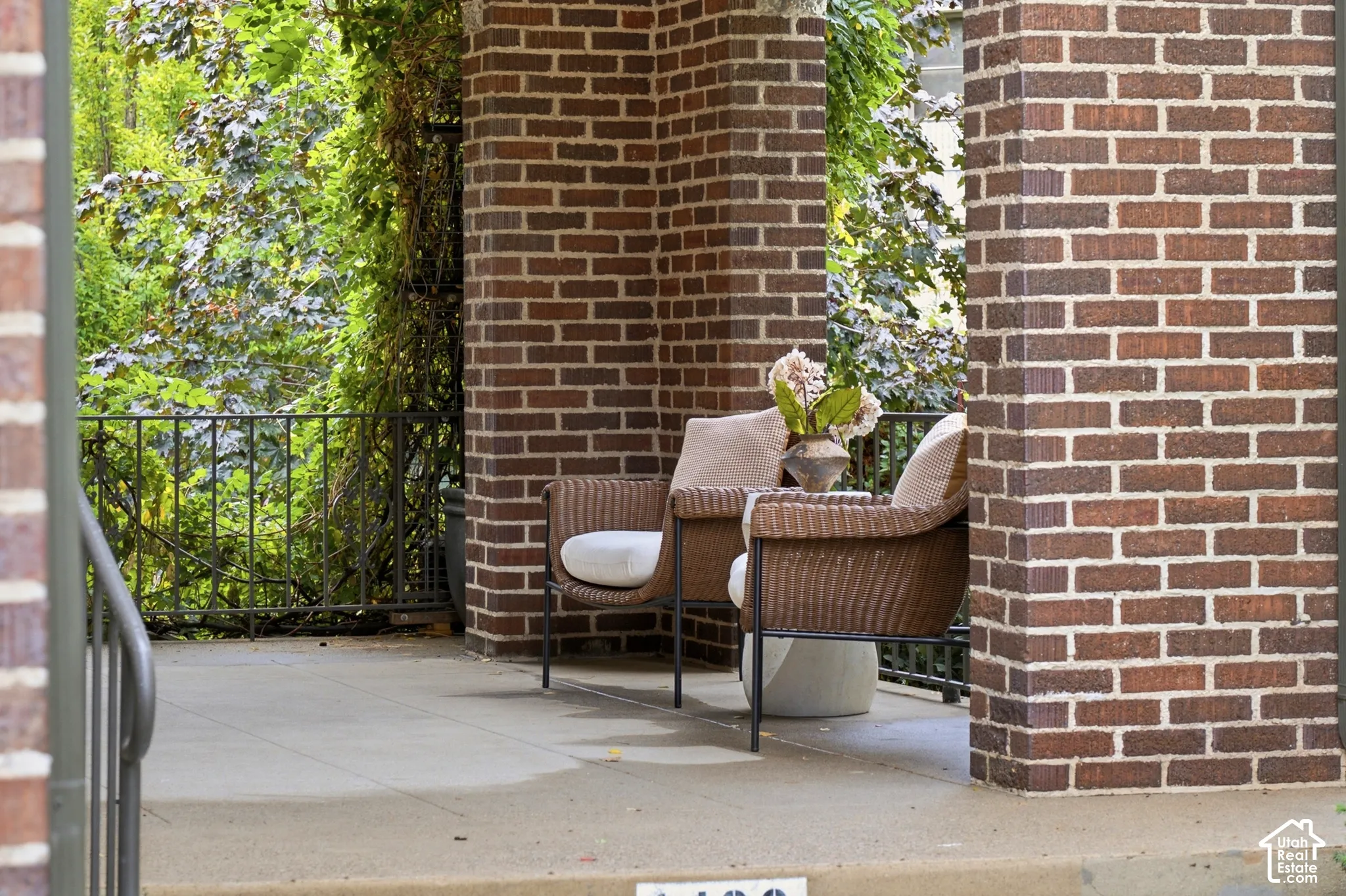 Brick exterior columns framing a concrete patio with a dark metal railing