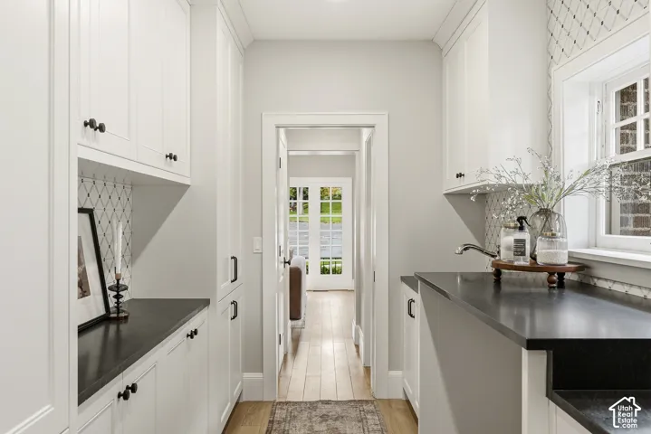 White cabinetry with bronze hardware, dark countertops, a window with exterior brick detail, and wood-finish flooring