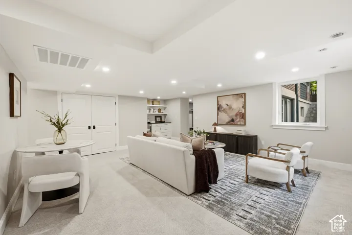 Recessed lighting, light-colored carpeting, built-in shelving, white double doors, and a window providing natural light to the backyard