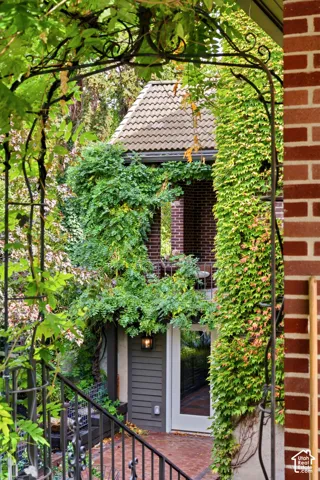 Wrought iron archway and railings over a brick paver patio, featuring a glass-paneled door, exterior wall lantern, and brick exterior with climbing vines