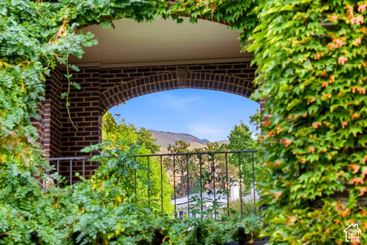 Brick arched opening with a metal railing, framed by lush foliage