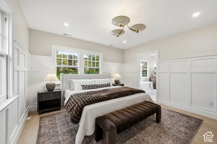 Primary Bedroom. A light-filled room with wood flooring, recessed lighting, and a contemporary ceiling fixture. The walls feature wainscotting and original double hung windows.