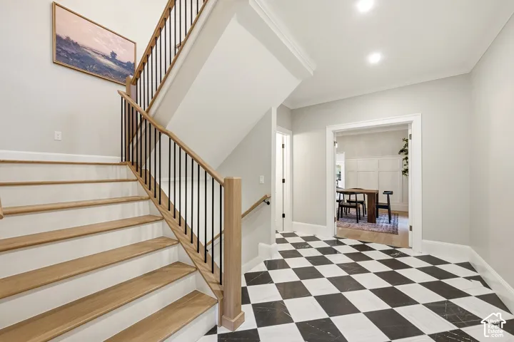 Checkered floor tiling, wood-finish staircase, black metal balusters, and recessed ceiling lighting, with view towards formal dining room