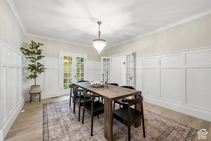 Crown molding, light wood-finish flooring, white wainscoting, French doors with multi-pane glass, and an antique crystal tiered chandelier