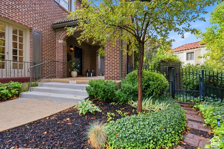 Brick exterior, arched entryway, concrete front steps with handrail, wrought iron fencing, and mature landscaping