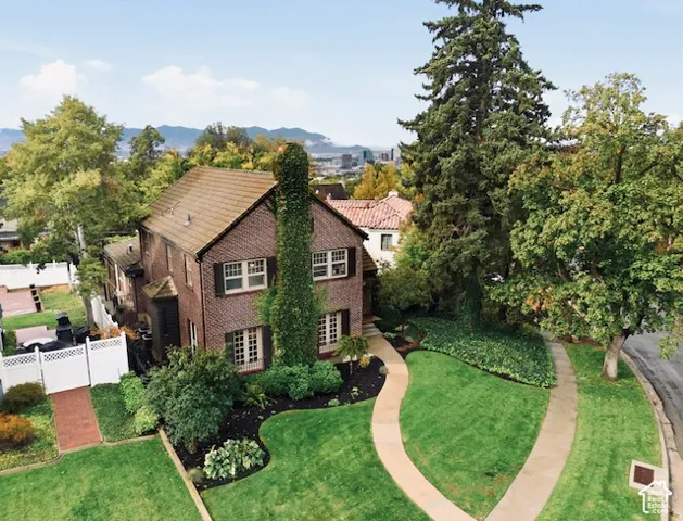 Multi-story brick exterior featuring a prominent chimney, shingle roof, white-framed multi-pane windows, and extensive mature landscaping