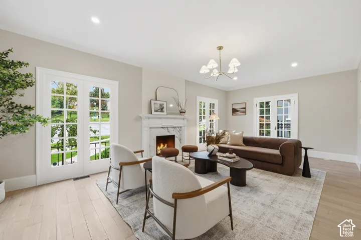 Elegant living room featuring beautiful chesnut oak wood floors, gas fireplace with marble surround, original mantel, and chandelier lighting. Four pairs of original French doors flank the room, bringing in vibrant scenery and abundant daylight