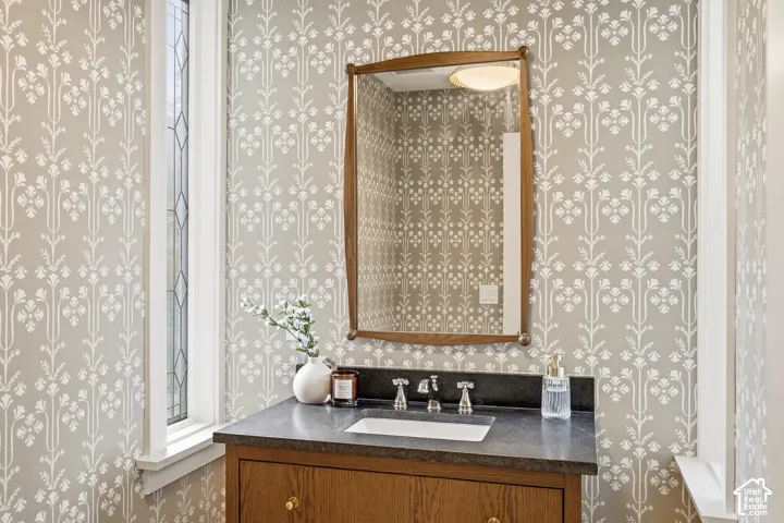 Family Powder Room with built-in wood vanity, brass hardware, undermount sink, black mist countertop, and decorative wall covering