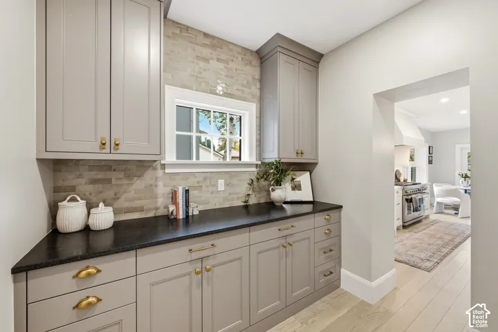 Butler's Pantry with built-in cabinetry, brass hardware, black mist countertops, and a subway tile backsplash