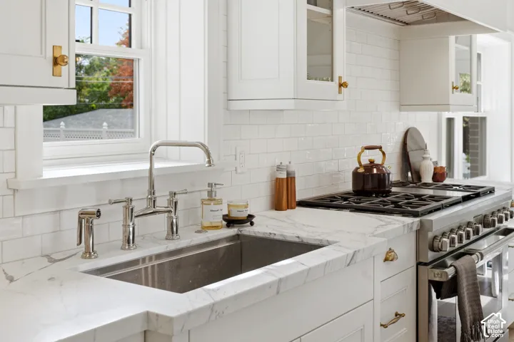 White shaker cabinetry, subway tile backsplash, stainless steel sink, polished nickel faucet, and professional-grade range