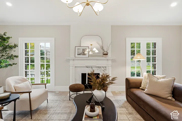 Spacious living area featuring a decorative fireplace with a marble surround, dual French doors, a prominent chandelier, and light wood-finish flooring