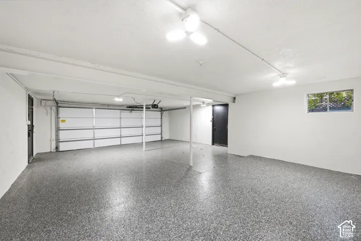 Spacious garage with an overhead door, light gray speckled flooring, white walls, and a single window