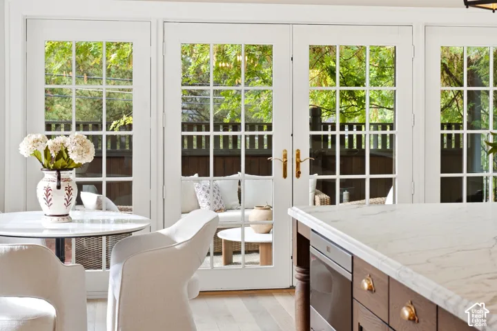 French doors with transom windows, light wood-finish flooring, island with a stone countertop, built-in appliance, and custom cabinetry with brass hardware