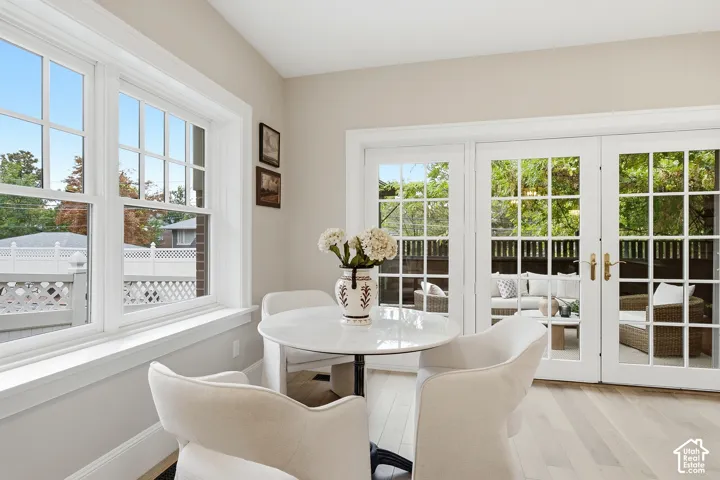 Wide plank wood-finish flooring, white grid-pattern windows, white grid-pattern French doors, and light-toned walls