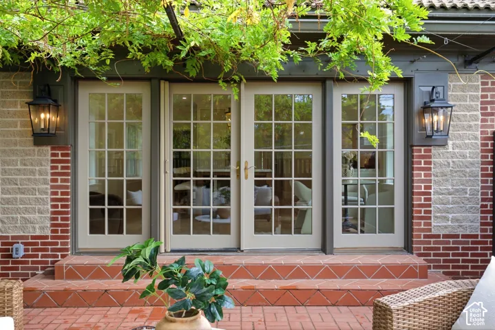 French Pella doors with divided lites, two-tone brick exterior, wall-mounted bronze lanterns, and a red brick patio with steps