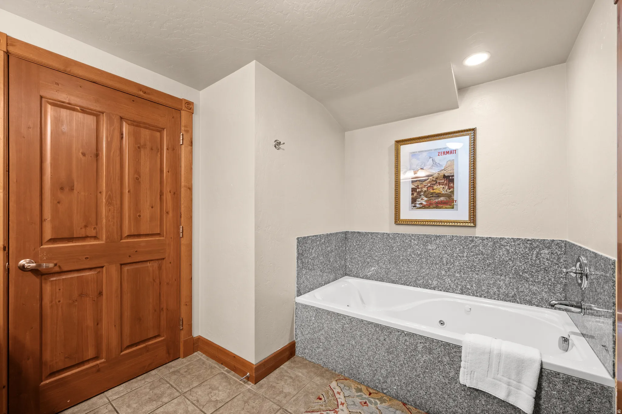Master bathroom featuring a soaking tub with tile surround, polished stone accent wall, white subway tile backsplash, and dual fixtures