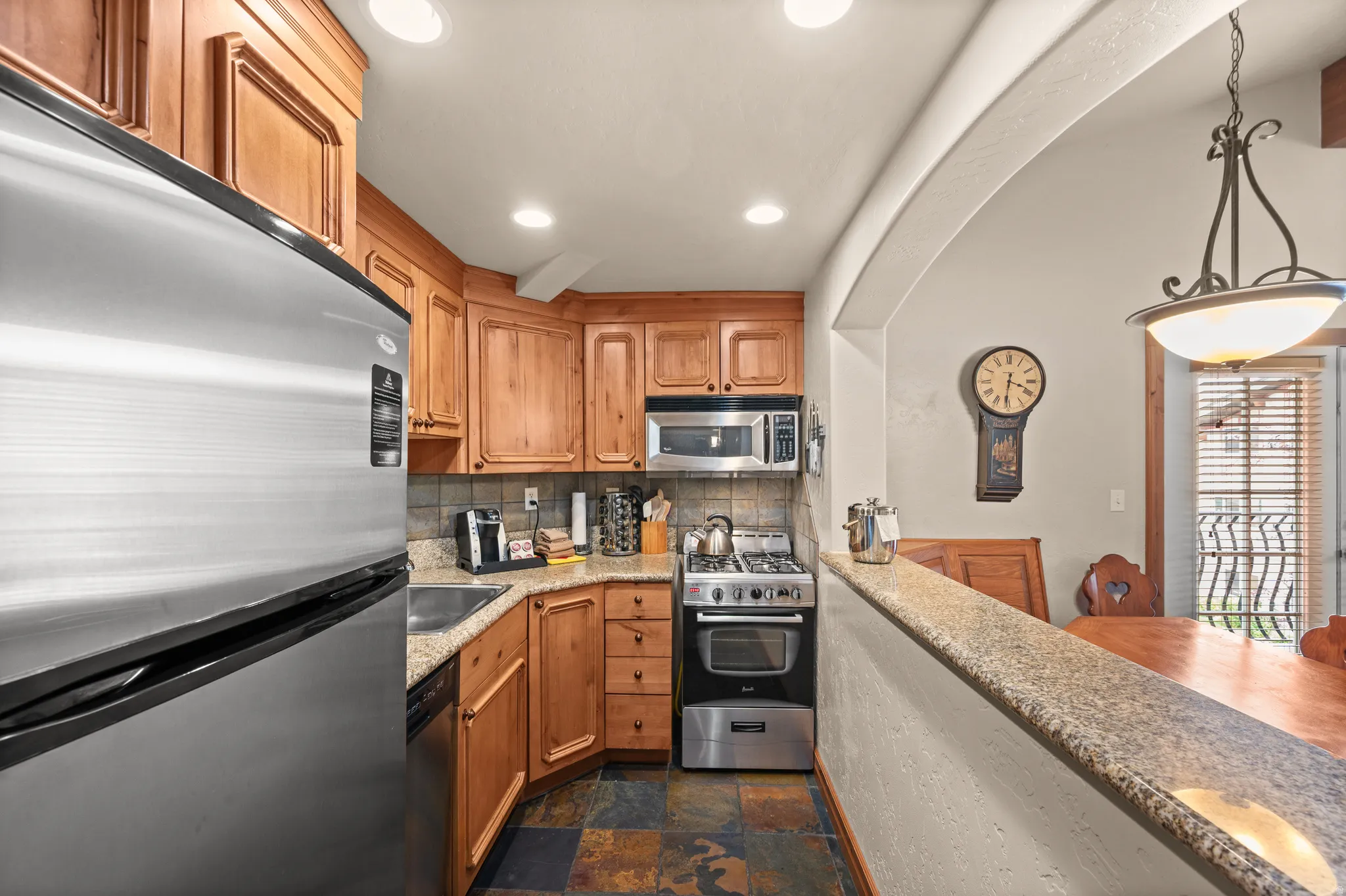 Wood cabinetry paired with stainless steel appliances, a tile backsplash, and stone-finish countertops