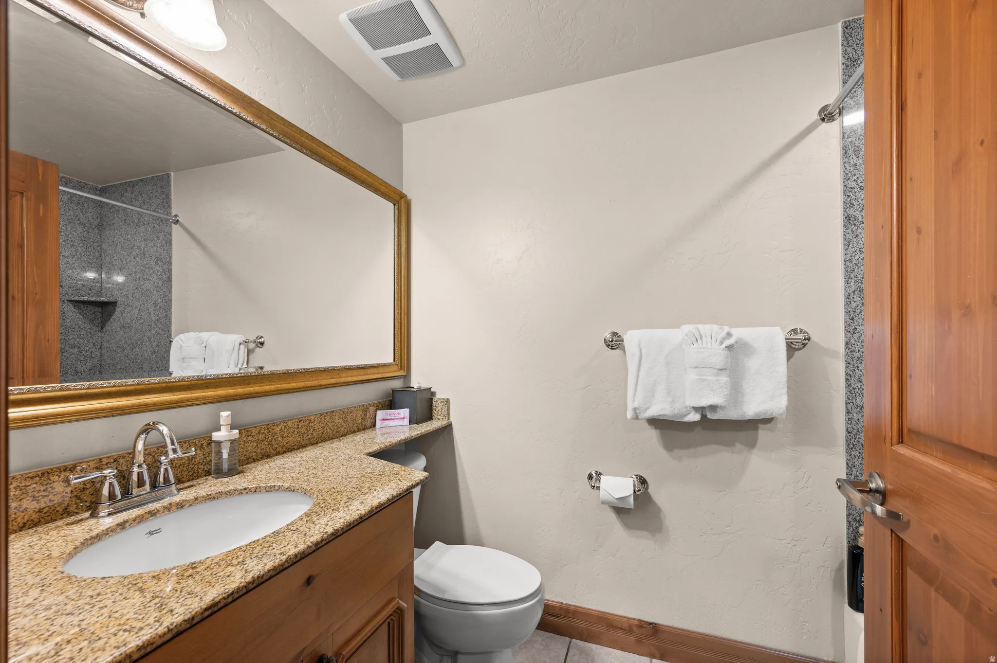 Spa-inspired bathroom featuring warm wood cabinetry with granite countertop, round undermount sink, and polished chrome fixtures
