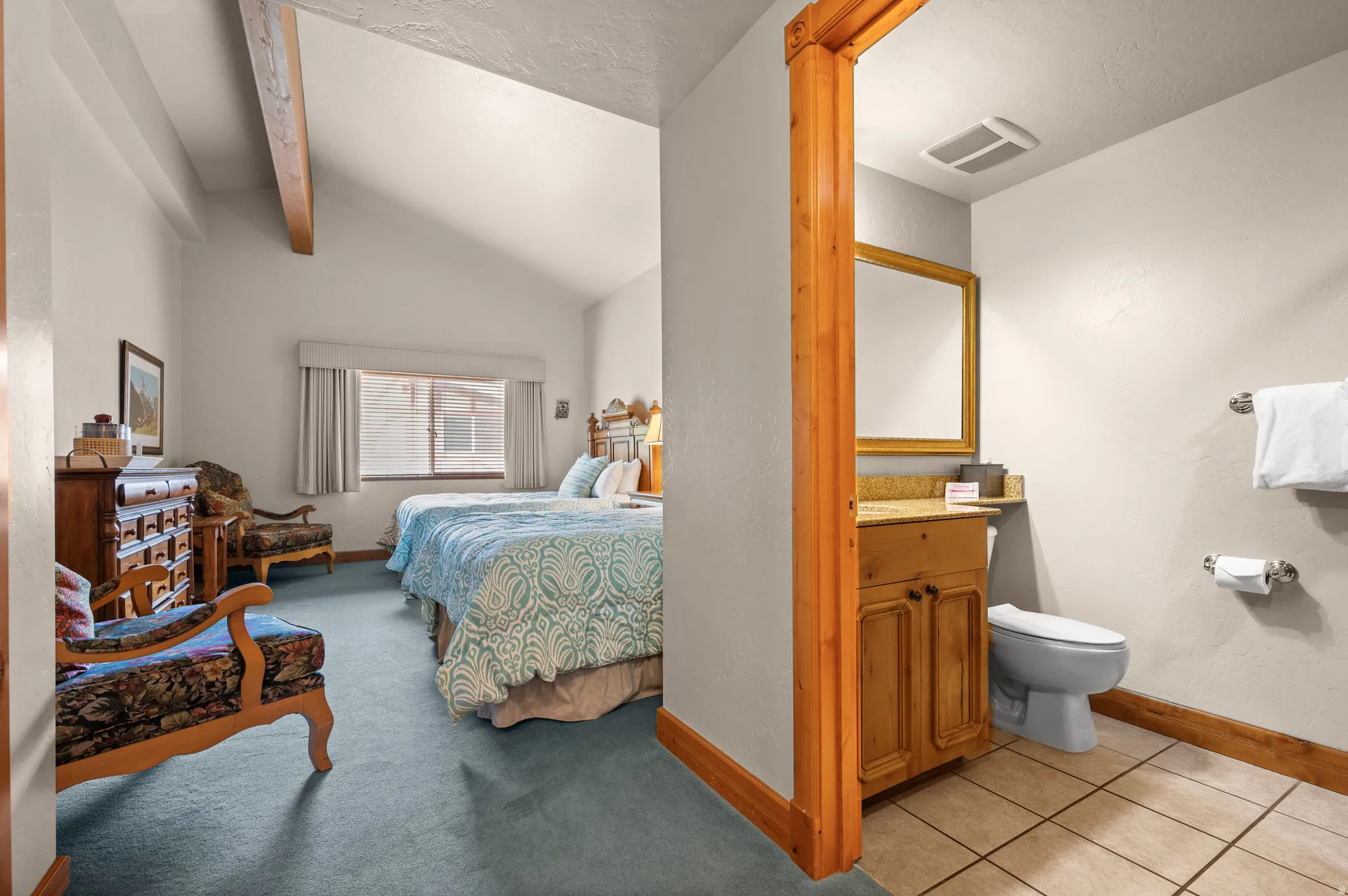 Primary Bedroom and En-Suite Bathroom featuring vaulted ceilings with exposed wood beam, ceramic tile flooring, wood vanity with integrated sink, and abundant natural light from multi-pane windows