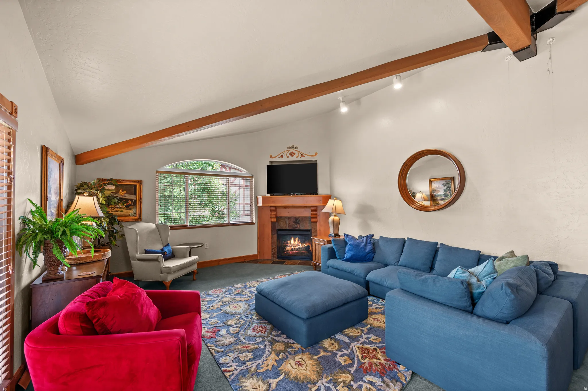 Spacious living room featuring exposed wood beam ceiling, wood-burning fireplace with wood mantel, built-in entertainment center, and large multi-pane windows with natural light