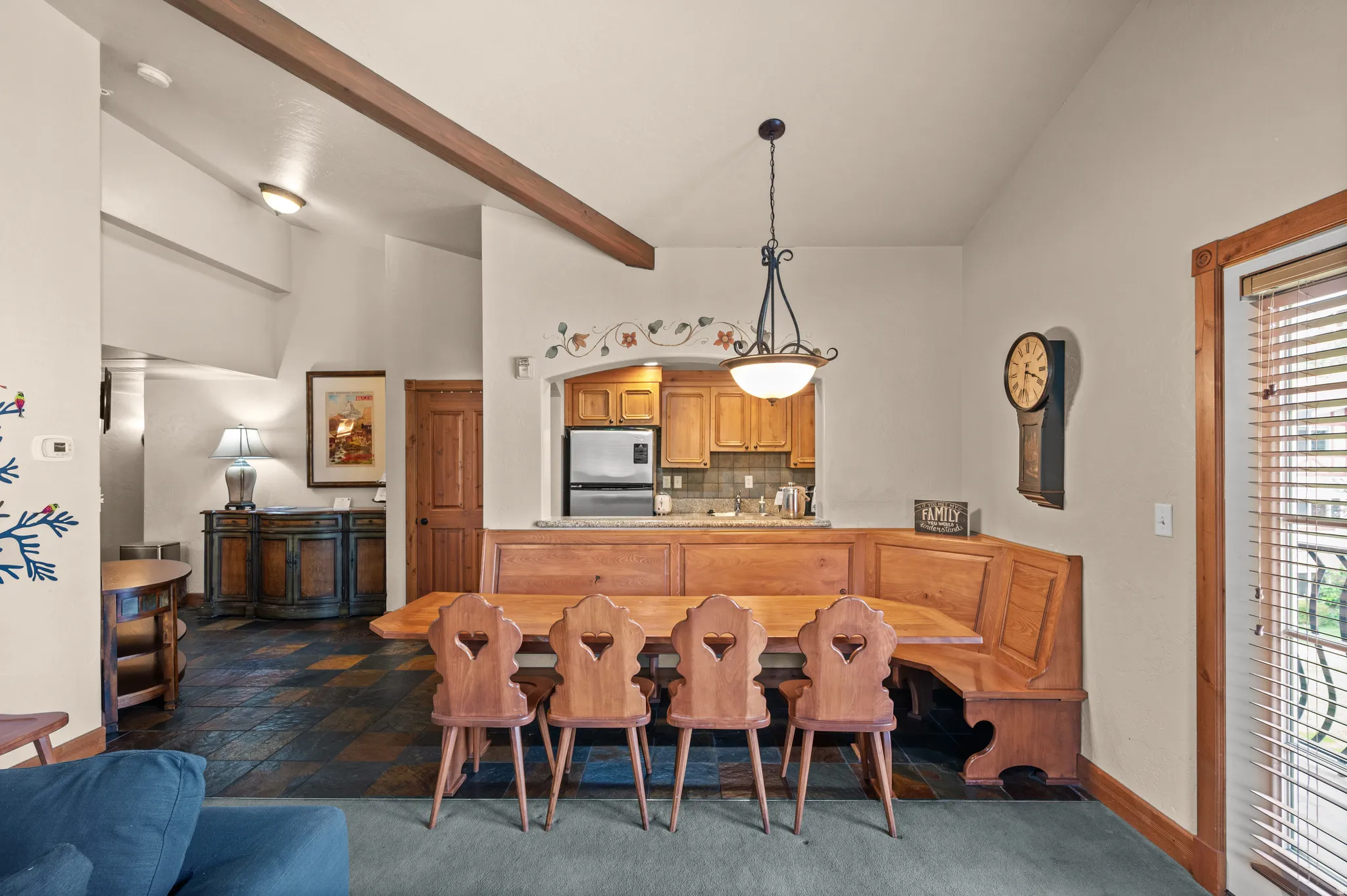 Vaulted ceilings with exposed beam, integrated dining banquette, wood-finish cabinetry, tile flooring, and a pass-through kitchen window