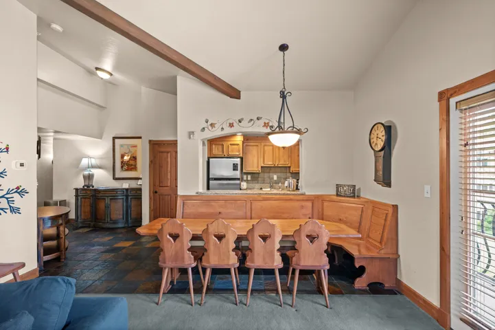 Vaulted ceilings with exposed beam, integrated dining banquette, wood-finish cabinetry, tile flooring, and a pass-through kitchen window