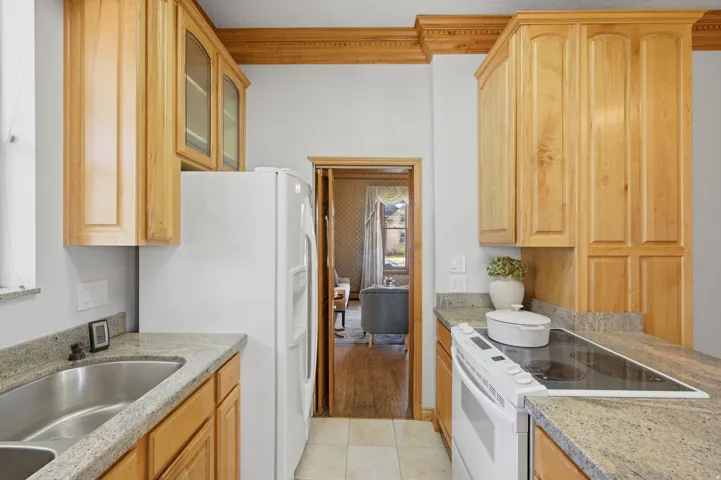 Well-appointed kitchen featuring light wood cabinetry, stone countertops, stainless steel double basin sink, and a built-in electric cooktop