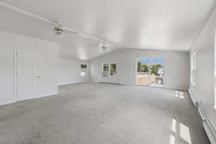 Vaulted ceilings, neutral-toned carpeting, multiple windows, and sliding glass doors