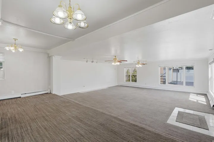 Spacious room featuring carpet flooring, multiple windows, two ceiling fans, and overhead lighting fixtures
