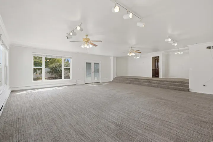 Expansive carpeted room featuring multiple ceiling fans, track lighting, and a raised platform