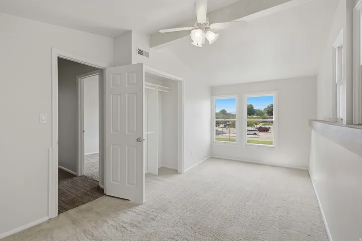 Vaulted ceiling with exposed beams, carpeted flooring, white interior doors, built-in closet, and natural light from multiple windows