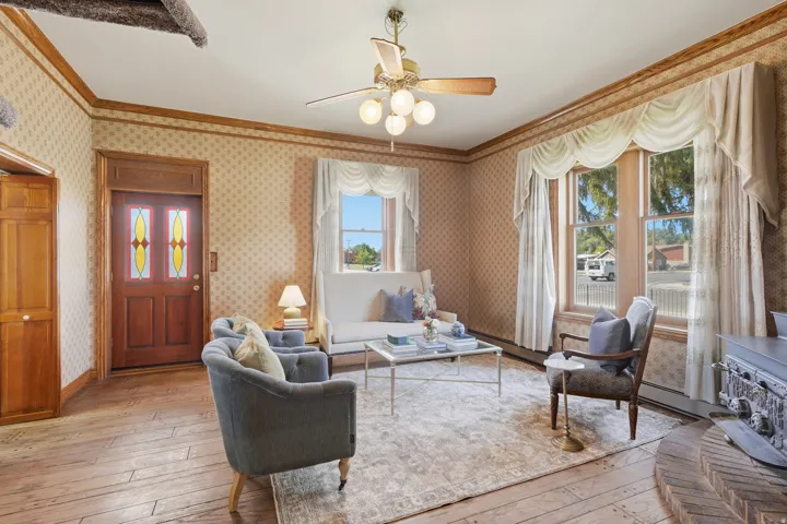 Wood-finish flooring, decorative wallpaper, wood trim, two large windows, and an ornate ceiling fan with lighting