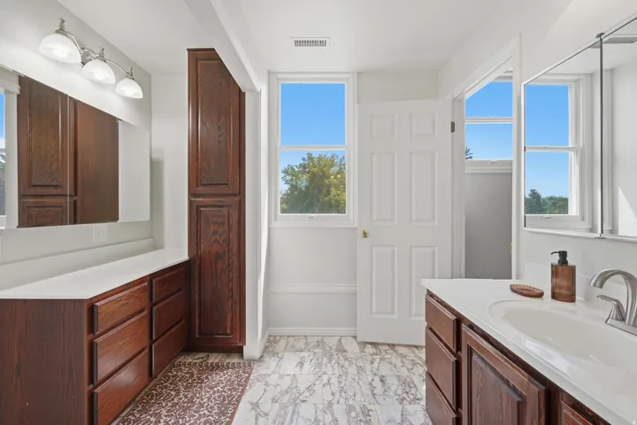Dual vanity sinks with white countertops, wood-finish cabinetry, and wall-mounted light fixtures