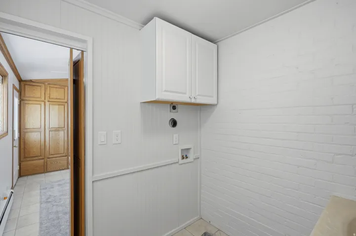 White upper cabinetry, white painted brick accent wall, white beadboard paneling, and tile flooring