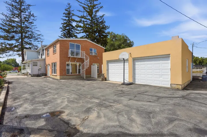 Brick exterior structure with white spiral staircase and balcony, stucco-finished detached garage with two garage doors