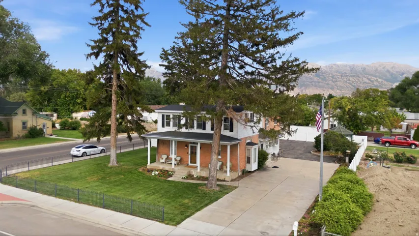 Brick exterior with white trim, covered front porch, a well-maintained lawn, and mature trees